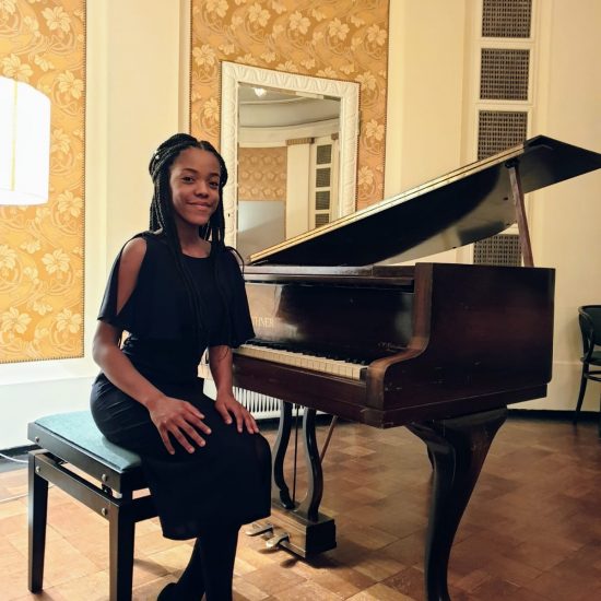 girl sitting at a baby grand piano, smiling at camera